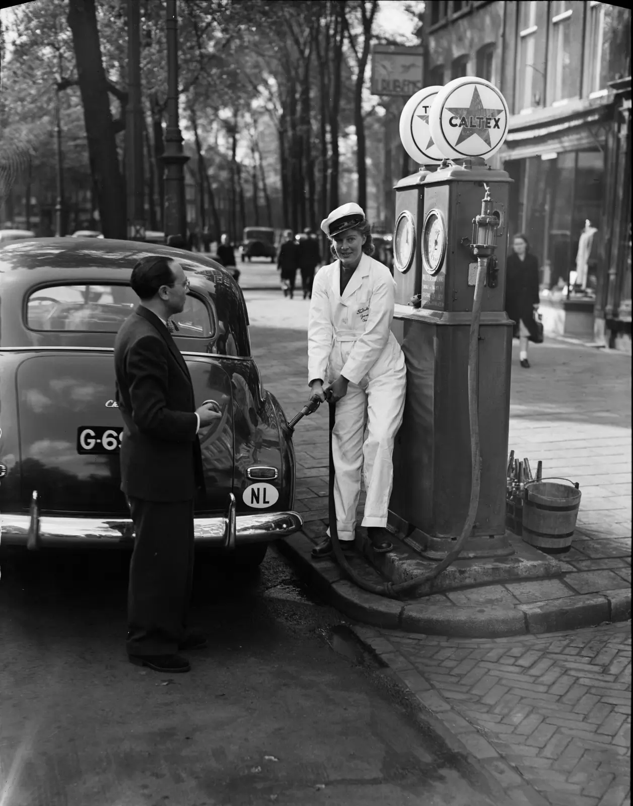 Pompbediende in wit uniform bij een Caltex-pomp in Amsterdam in 1947