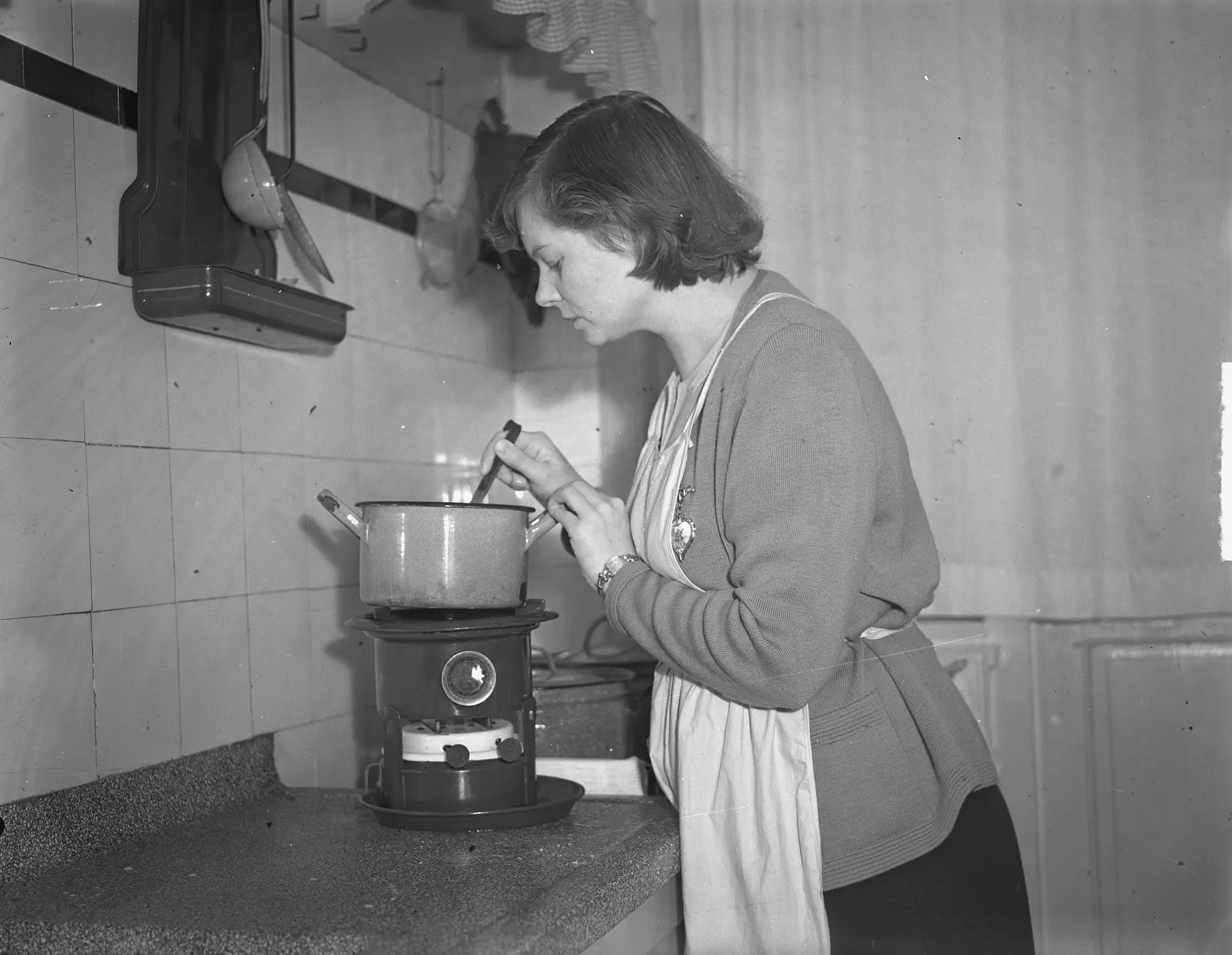 Een vrouw roert in 1950 in een pan op een petroleumstel