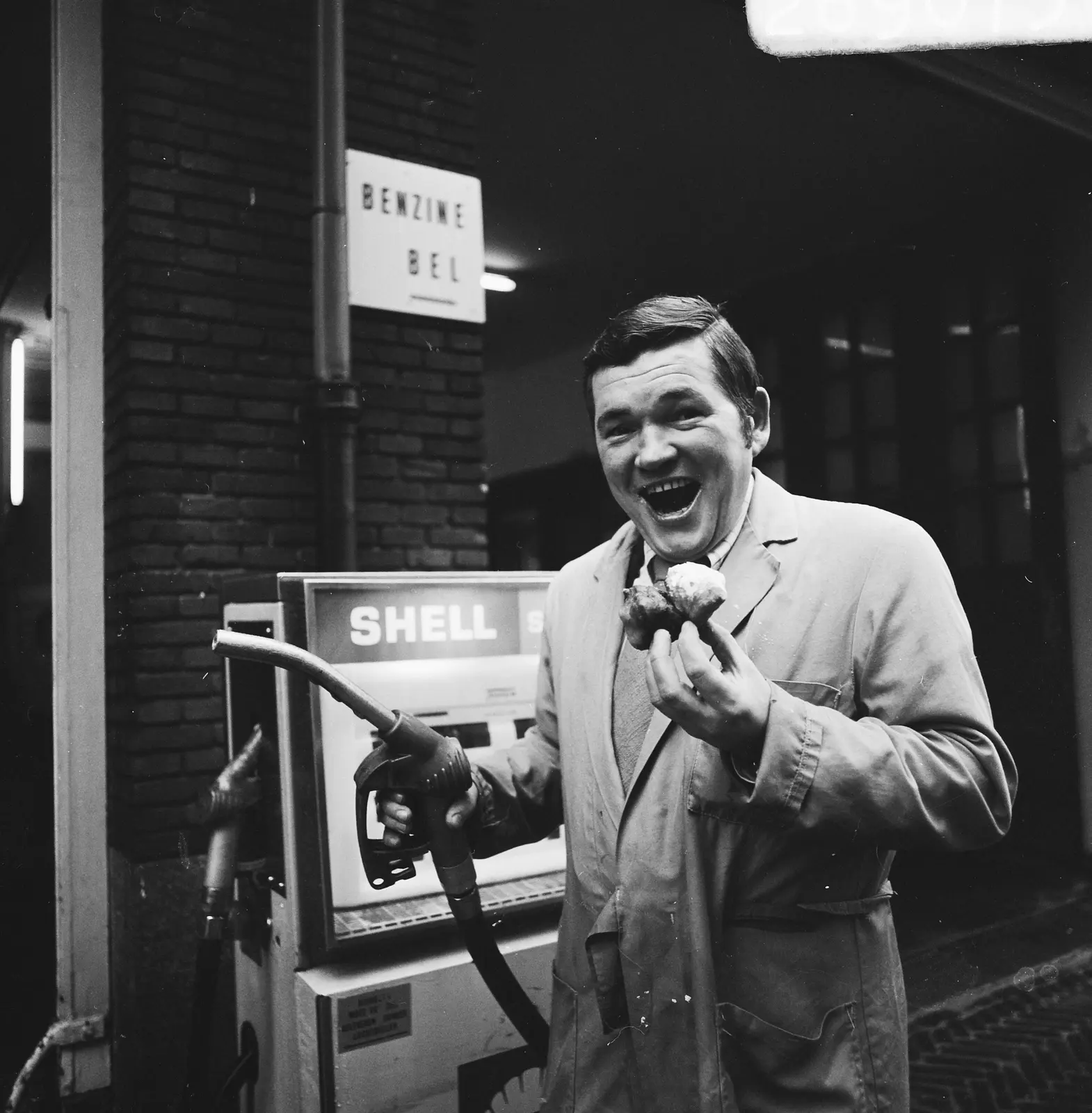 Een lachende pompbediende houdt in 1973 een vulpistool en een oliebol vast bij een Shell-pomp