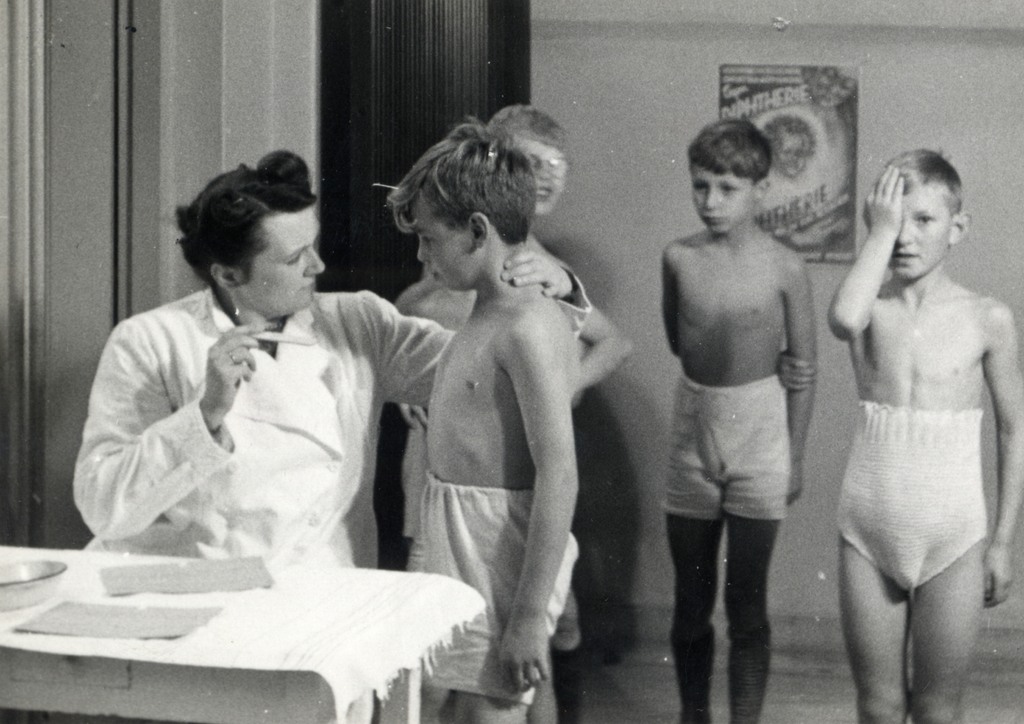 A school doctor examines a boy while other pupils wait